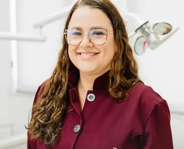Dra. Fabíola Cassiano de jaleco bordô, sorrindo no consultório.