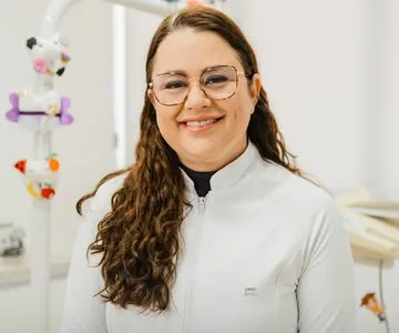 Dra. Fabíola Cassiano de jaleco branco, sorrindo no consultório.